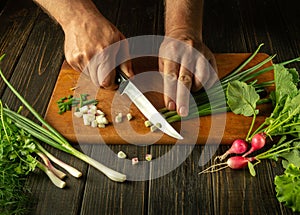 The cook cuts the onion with a knife on the kitchen cutting board. Vegetarian products or fresh vegetables on the kitchen table