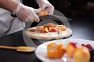 The cook cuts the persimmons and nectarines into slices. Assorted fruits and berries are cut into pieces. Unrecognizable photo.