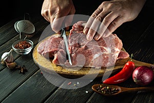 The cook cuts raw meat steak with a knife on the wooden cutting board of the restaurant kitchen. The concept of the process of