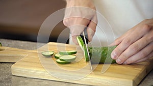 The cook cuts a spring salad of tomatoes, cucumbers, greens and mixes. Man cutting cucumber for salad on wooden cutting