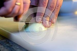 Cook cuts white onions with a knife on a white board