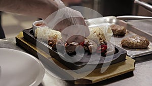 A cook decorates a dish with meat and pita bread in a metal tray.