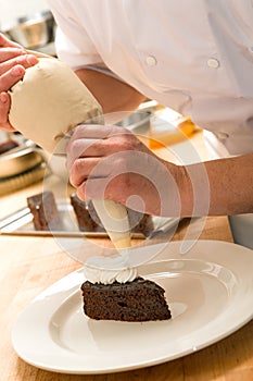 Cook decorating cake with whipped cream