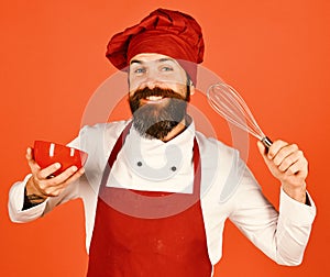 Cook with excited face in burgundy hat and apron holds bowl and whisk. Chef with red plate and whipping utensil. Man or