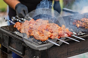 The cook fries juicy steaming meat on a charcoal grill. Food and cooking equipment at a street food festival