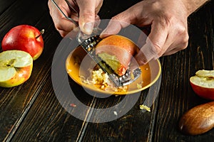 A cook grates a raw apple with a grater on a black kitchen table. The concept of a dietary dish or dessert. Place for ads