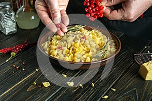The cook hands add red viburnum to a plate of pasta. Work environment on a kitchen table in a restaurant. Delicious pasta with