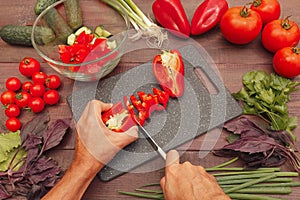 Cook hands cut fresh bellpepper for salad on wooden table photo