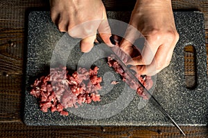 Cook hands cut red meat on the board. nearby are tomatoes, onion, butter