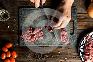 Cook hands cut red meat on the board. nearby are tomatoes, onion, butter