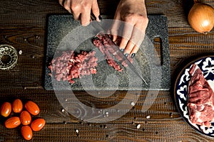 Cook hands cut red meat on the board. nearby are tomatoes, onion, butter