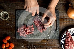Cook hands cut red meat on the board. nearby are tomatoes, onion, butter