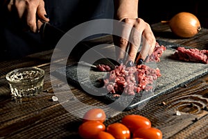 Cook hands cut red meat on the board. nearby are tomatoes, onion, butter