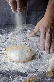 Cook hands kneading dough, sprinkling piece of dough with white wheat flour