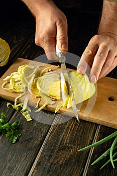 The cook hands use a knife to cut fresh cabbage on a cutting board to prepare a vitamin salad. Delicious peasant food. Copy space