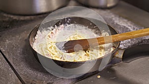 Cook holding stirring spaghetti with cheese sauce and chopped bacon frying in hot pan