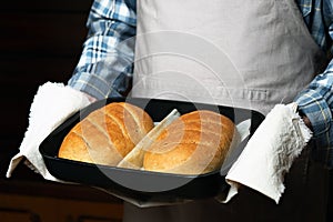 the cook holds a baking sheet with loaves of bread.