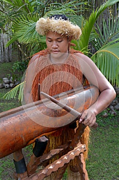 Cook Islander man plays music on a large wooden log Pate drum in