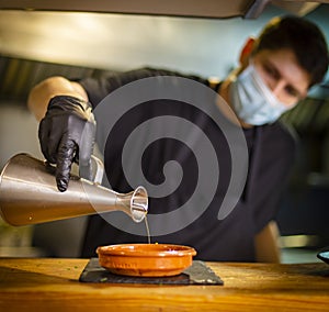 cook in the kitchen of a restaurant adding oil to a dish