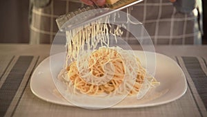 The cook in the kitchen rubs hard cheese into a plate of pasta with freshly prepared Italian pasta rubs cheese. With