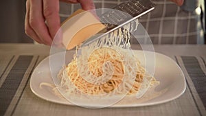 The cook in the kitchen rubs hard cheese into a plate of pasta with freshly prepared Italian pasta rubs cheese. With