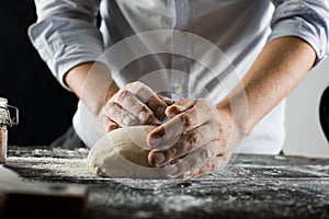 Cook kneads dough with flour on kitchen table