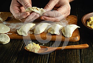 The cook makes dumplings from dough and potatoes with his hands. The concept of preparing delicious dumplings on the kitchen table