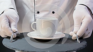 Cook man hold tray with cup tea or coffee on black backgrouind.