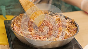 Cook mixes finely chopped pork steak and onions during stewing in frying pan