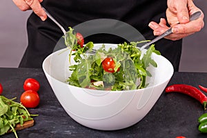 The cook mixes fresh vegetable salad with mozzarella cheese in a bowl