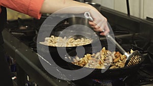 Cook mixes and fried meat dish in a frying pan or skillet in restaurant kitchen on gas stove in slow motion