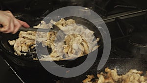 Cook mixes pieces of roasted chicken meat in a frying pan or skillet in restaurant kitchen on gas stove in slow motion