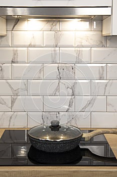 Cook pan at modern kitchen induction cooker hob and wooden counter and white tile backsplash