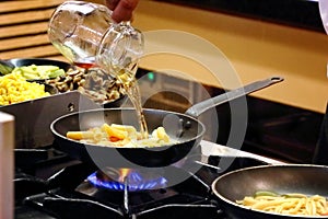 Cook pouring sauce from a jug into a bowl with pasta