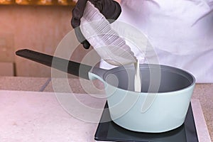 Cook pours the cream from the bowl into the saucepan to reheat. Hands in black rubber gloves close-up.