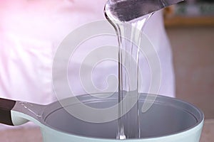 Cook pours the liquid glycerin into the saucepan to reheat. Close-up view.