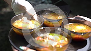 The cook pours meat soup in a cast-iron cauldron on plates. Slow motion