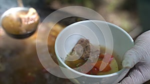 The cook pours meat soup in a cast-iron cauldron on plates. Slow motion