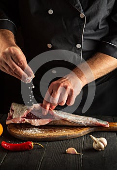 The cook prepares fresh fish sprinkling salt. Preparing to chef fish food. Working environment in the restaurant kitchen
