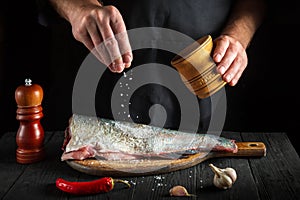 The cook prepares fresh fish sprinkling salt. Preparing to chef fish food. Working environment in the restaurant kitchen