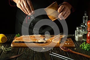 The cook prepares fresh salmon fish, trout smorgus, sprinkling the ingredients with salt. Getting ready to prepare a fish dish