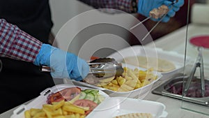 Cook prepares lunch boxes with Greek kalamaki dish with souvlaki meat, fries and vegetables