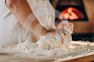 The cook prepares the pizza dough. A man kneads the dough with his hands for making pizza in the oven.