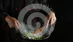 The cook prepares vegetables in a frying pan. The concept of cooking healthy vegetarian food and meals on a black background. Free