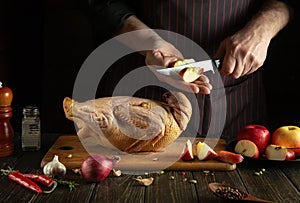 The cook is preparing duck for lunch. Raw duck with apples and spices on the kitchen table. Chef cuts an apple