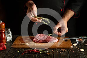 The cook is preparing a meat steak. Adding rosemary to lamb before grilling