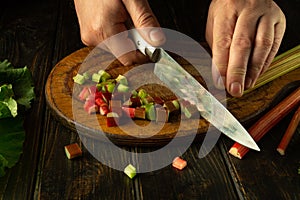 The cook is preparing a salad on the kitchen table. Close-up of a chef hands slicing fresh rhubarb stems with a knife