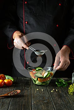 The cook is preparing a vegetable salad for lunch in the kitchen. Adding paprika to vitamin salad. Space for a recipe on a dark