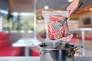 Cook puts the meat packed in a vacuum for low-temperature cooking in a saucepan