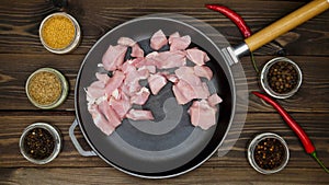 The cook puts the meat on the pan. Diced pork in a cast iron skillet. A metal frying pan on a wooden table surrounded by spices